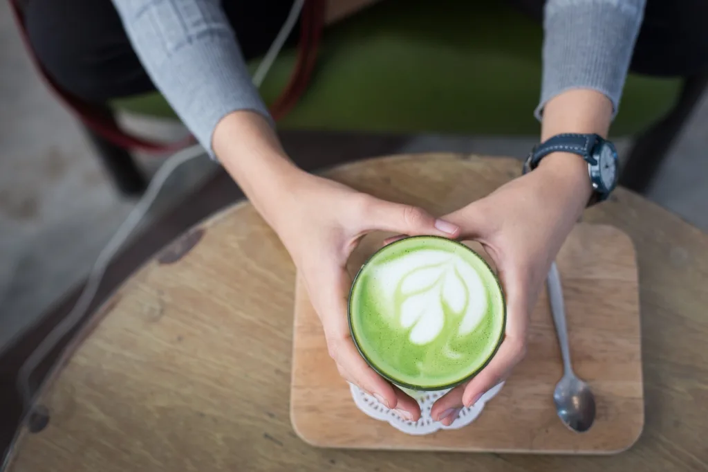mãos segurando uma xicara de matcha com leite.