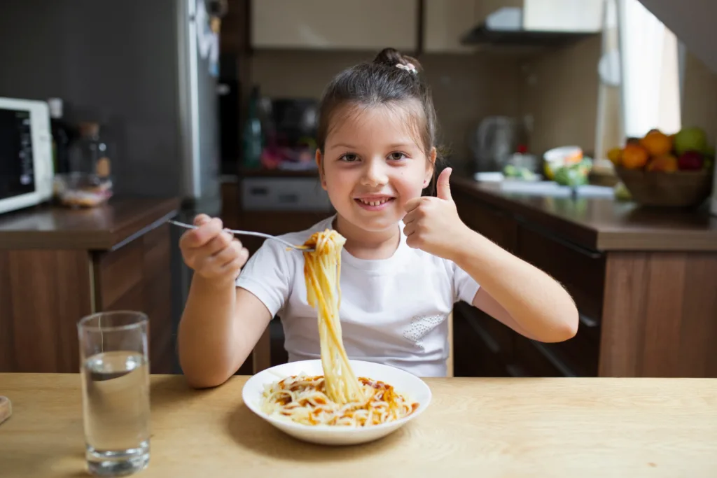 criança feliz com seu prato de macarrão.