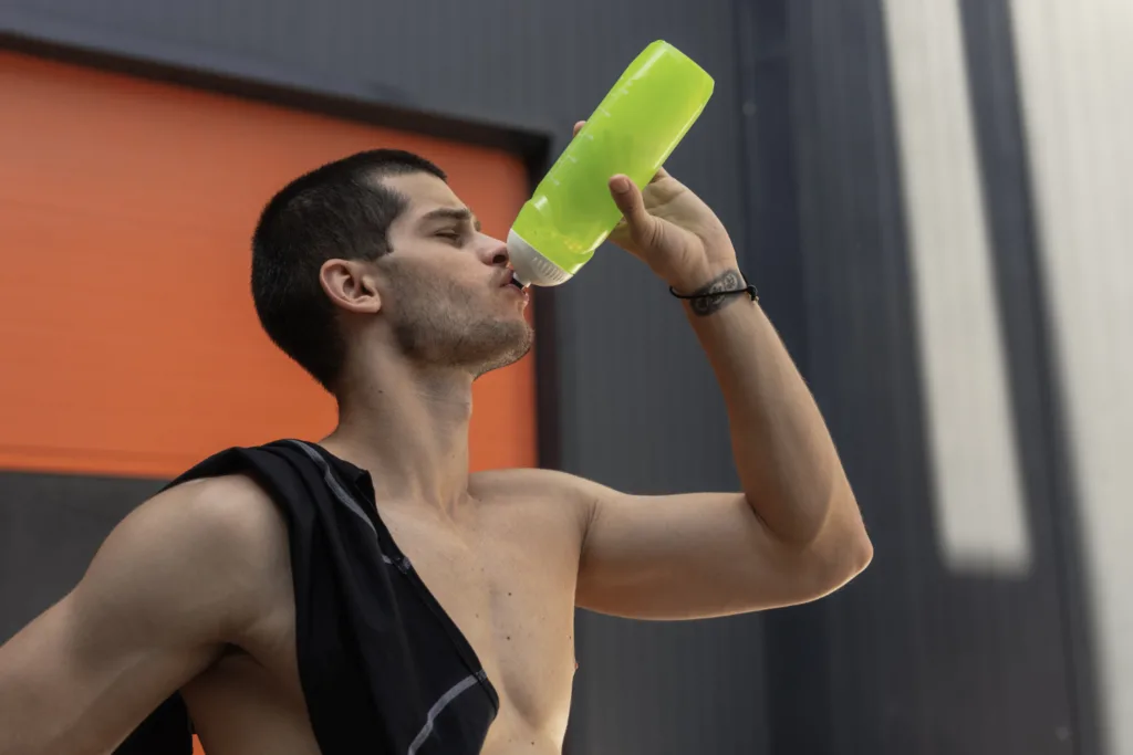 jovem atleta sem camisa se hidratando com uma garrafa cor verde limão.
