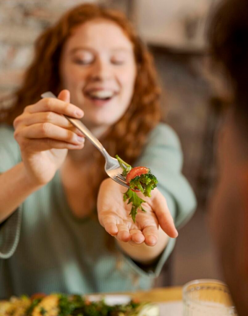uma jovem oferecendo uma porção de salada em um garfo, para o seu parceiro.