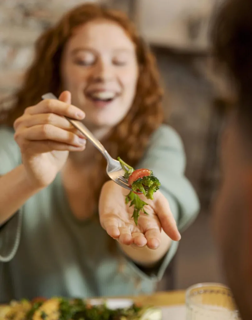 uma jovem oferecendo uma porção de salada em um garfo, para o seu parceiro.