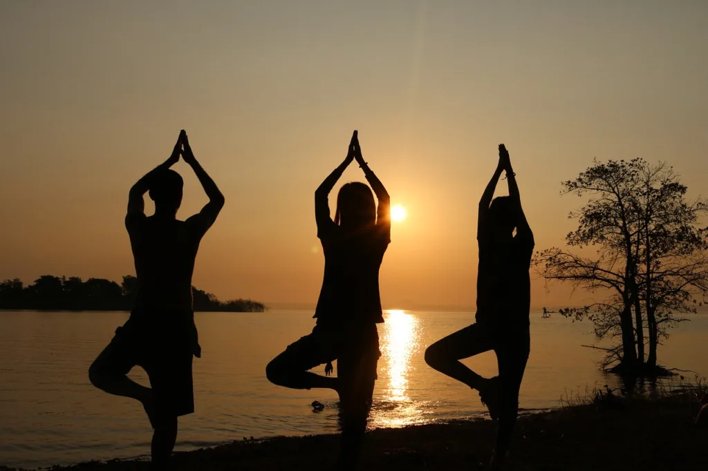 silhuetas de três praticantes de yoga num por do sol de um lago.