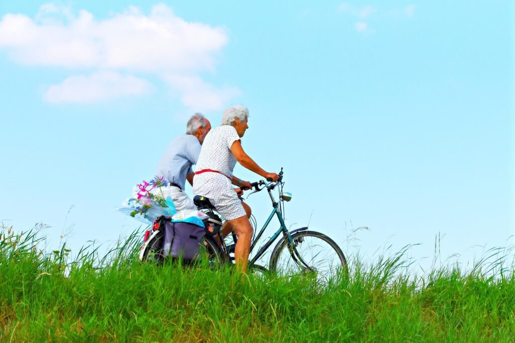 um casal de idosos se exercitando numa bicicleta ao ar livre.