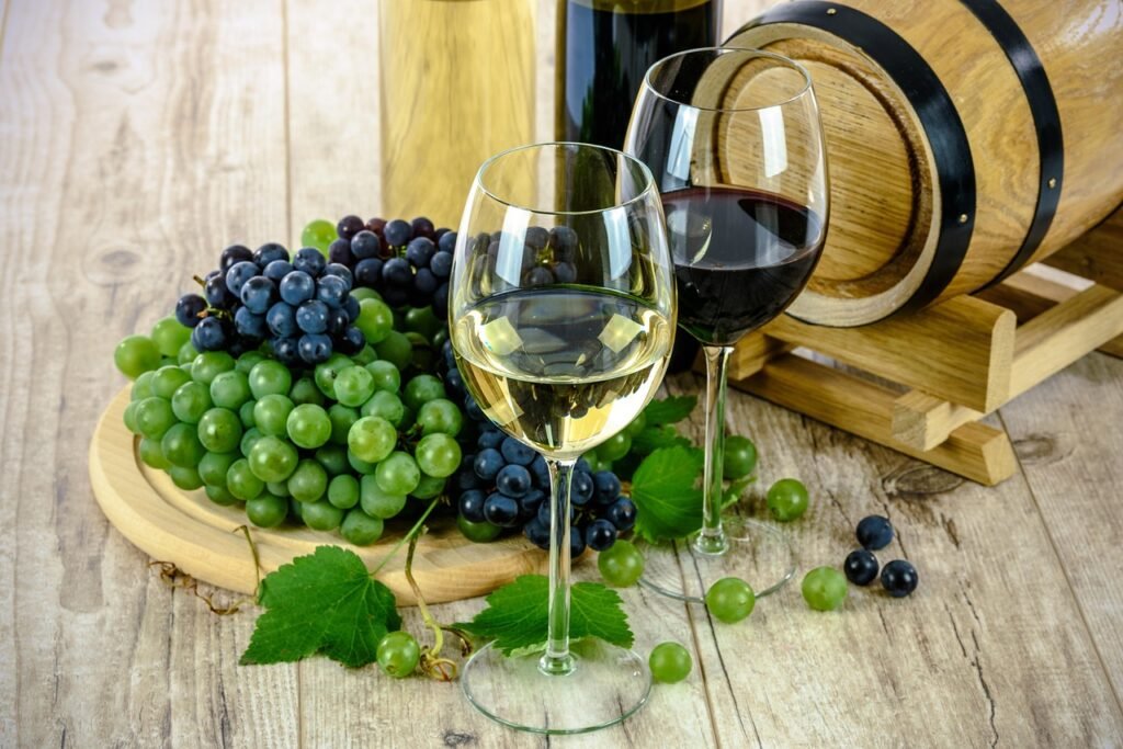 duas tacas de vinhos branco e tinto, acompanhada por um tonel e vários cachos de uvas.