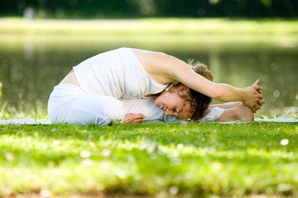 Uma jovem sentada ao ar livre em posição de yoga.