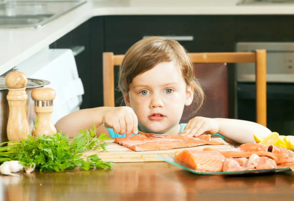 linda criança comendo file de salmão.
