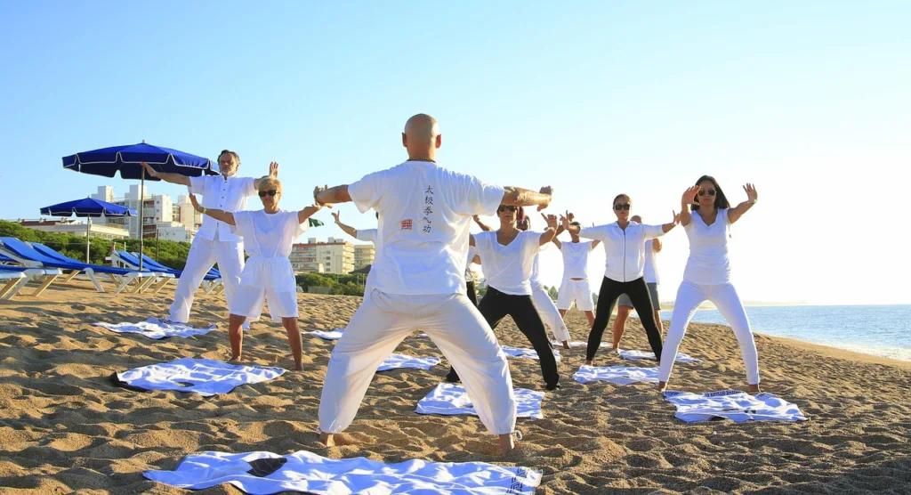 grupo de pessoas de roupas brancas praticando yoga numa praia.