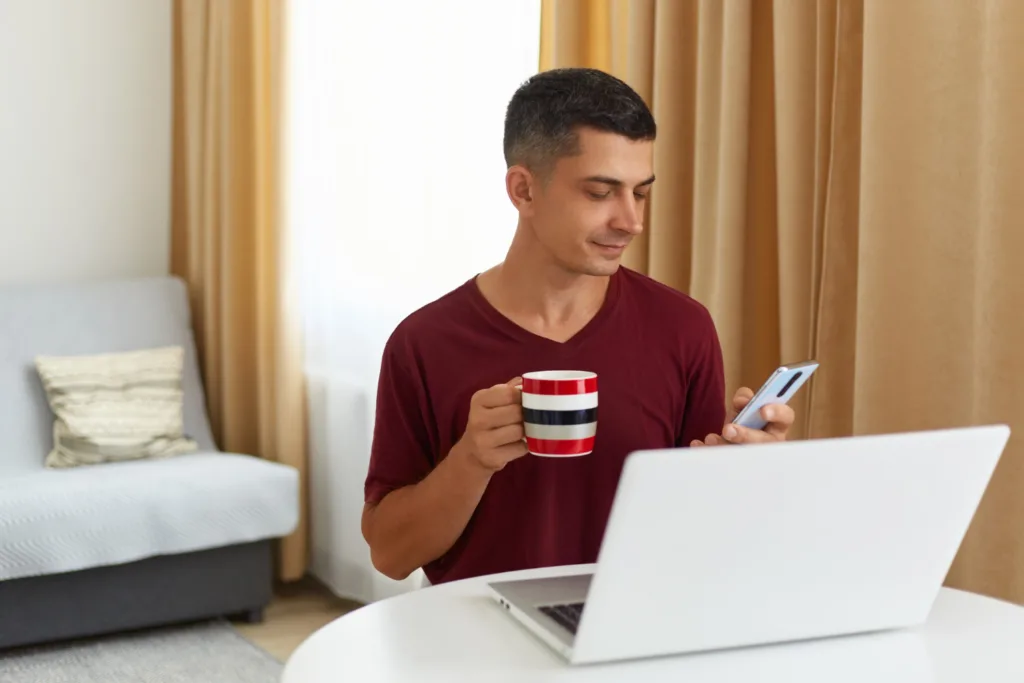 homem usando notebook e celular em um quarto