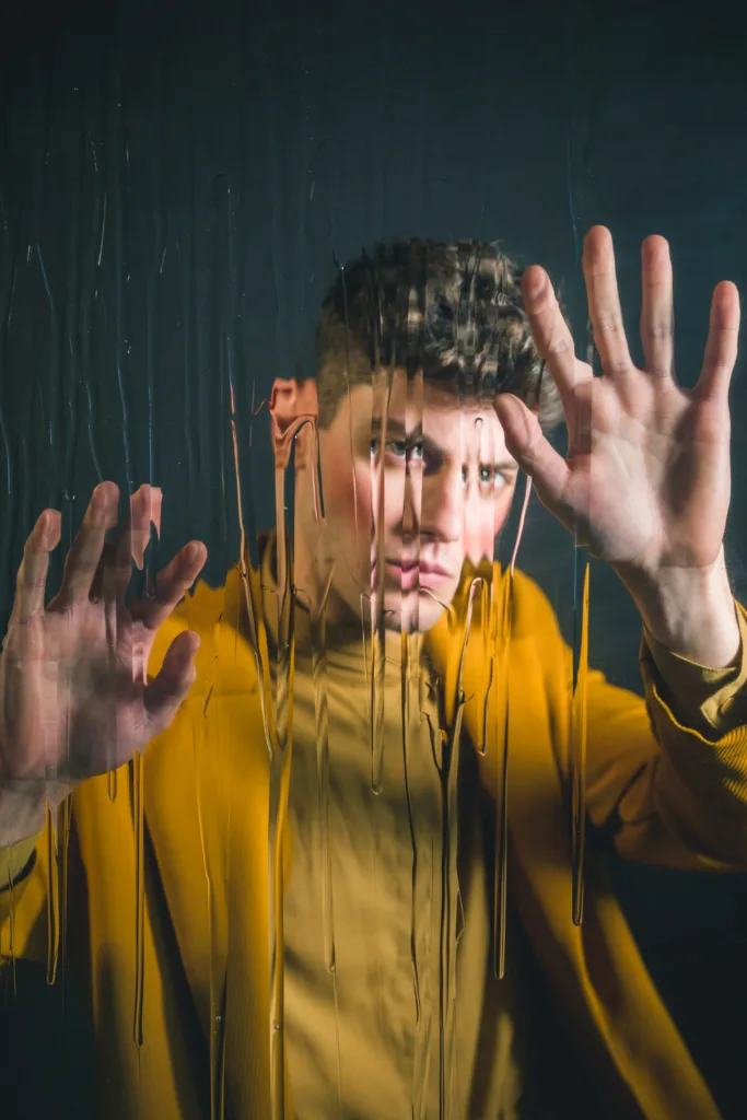 homen com disturbios olhando atraves de um vidro da janela nun dia chuvoso.