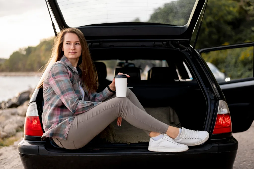 uma jovem sentada no lugar de bagagem do carro a espera de combustivel.