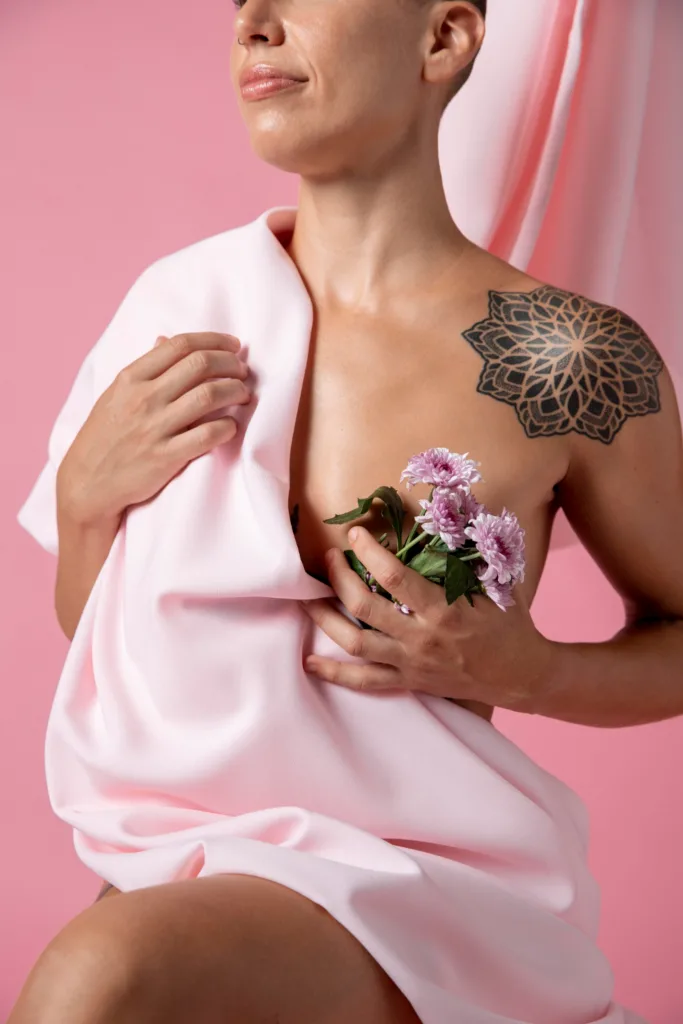 mulher com tatuagem tribal no ombro esquerdo, coberta com uma toalha e mostrando um bouqquet de flores no seio esquerdo