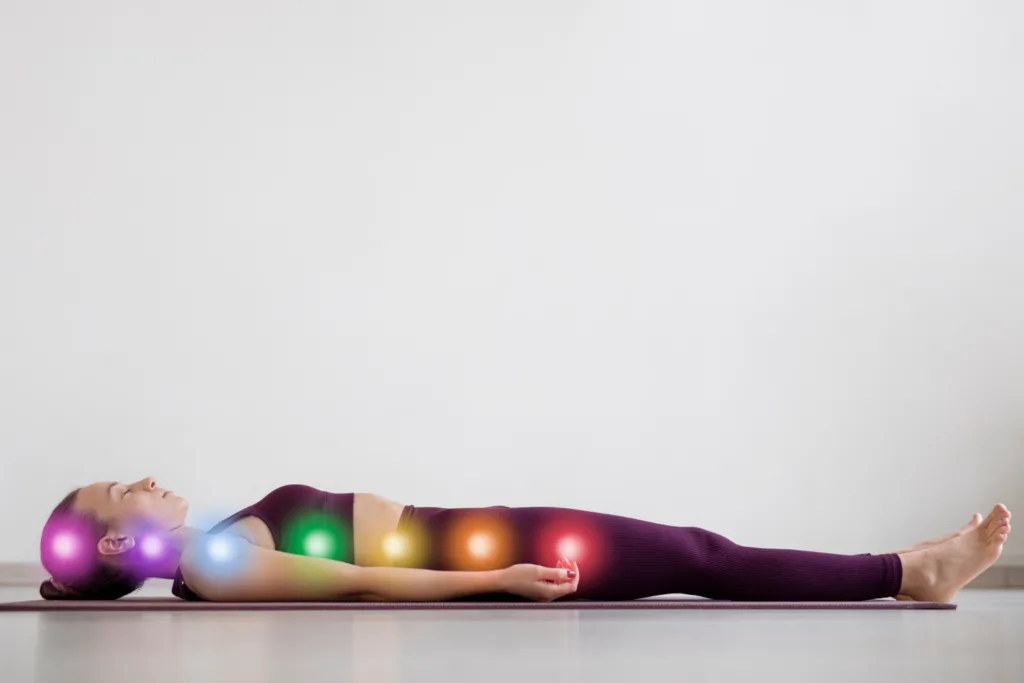 Jovem em trajes de yoga, deitada, discos de cores indicando os chacras.