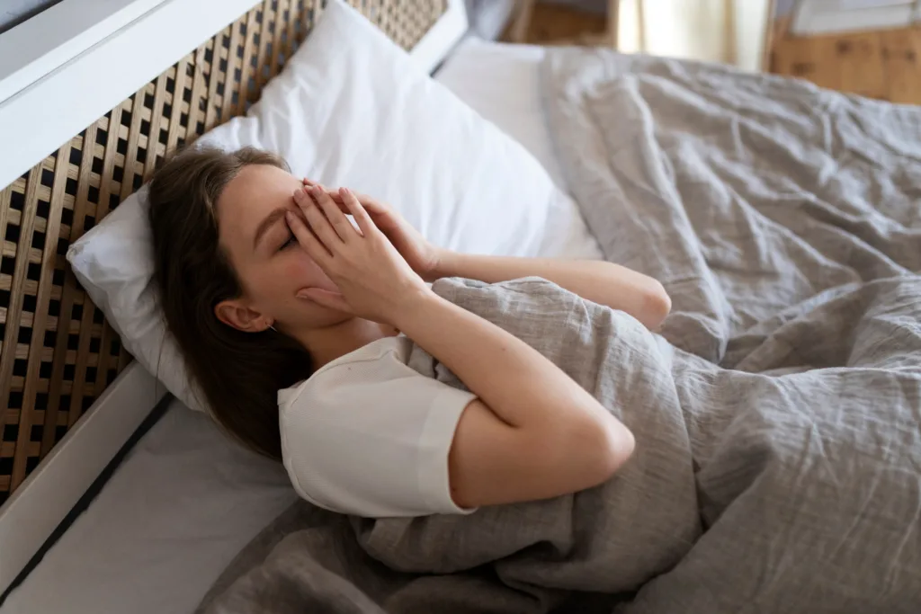 mulher deitada na cama com as mãos nos olhos, mostrando dificuldade de dormir.
