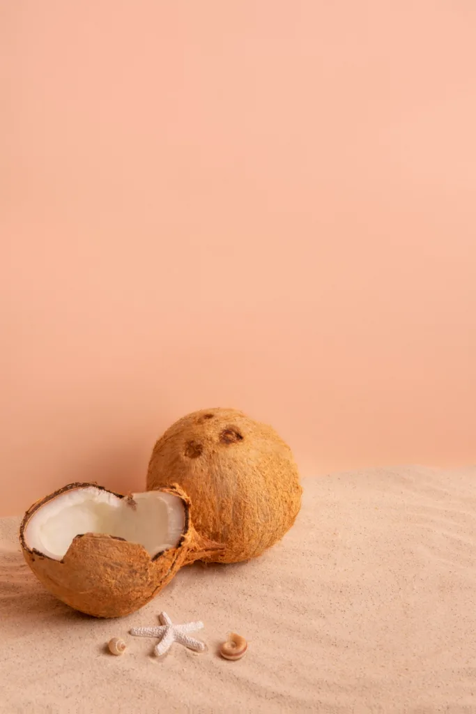 um coco inteiro seco, metade  de outro e pedacos pequenos, em um fundo cor de salmao.