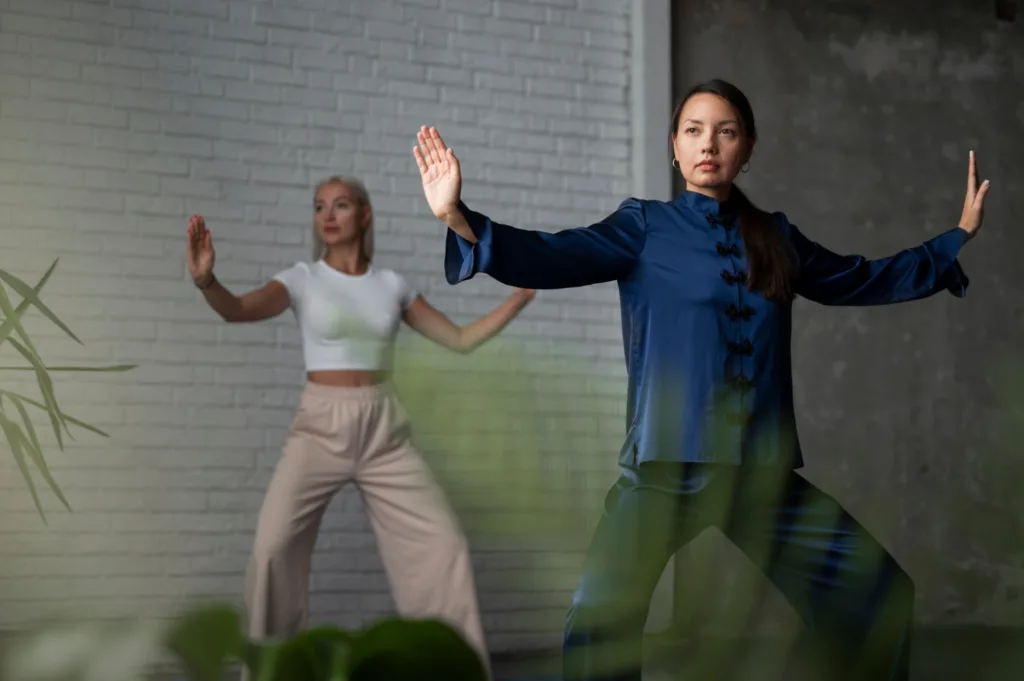 Uma mulher ocidental e outra oriental, praticando tai chi em um jardim.
