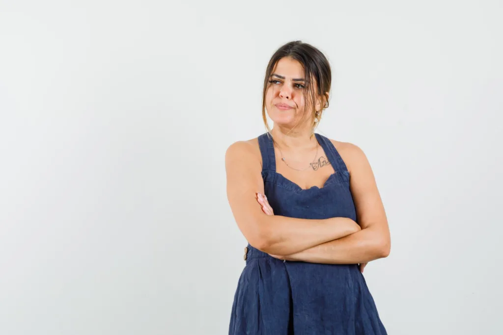 mulher com um vestido azul de alça, em um fundo branco, com uma expressão de desgosto.