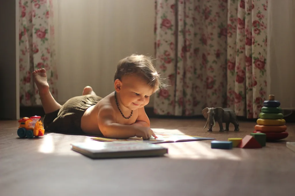 Menino deitado no chão folheando livros infantis.