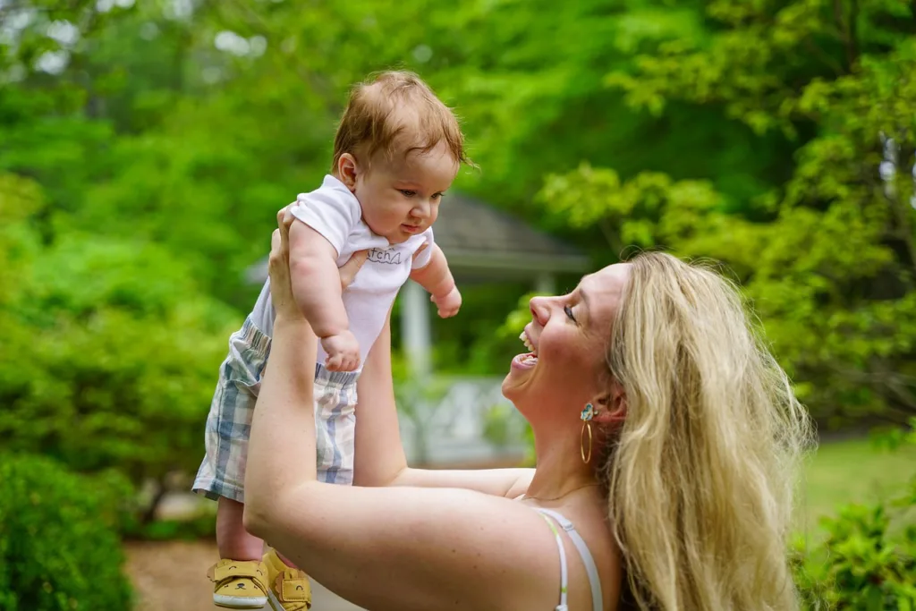 jovem mãe elevando seu filho bebe pelos bracos, ao ar livre.