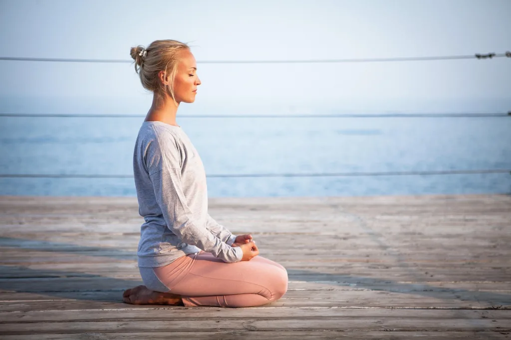 mulher praticante de yoga numa posição sentada sobre as pernas e mãos no colo.