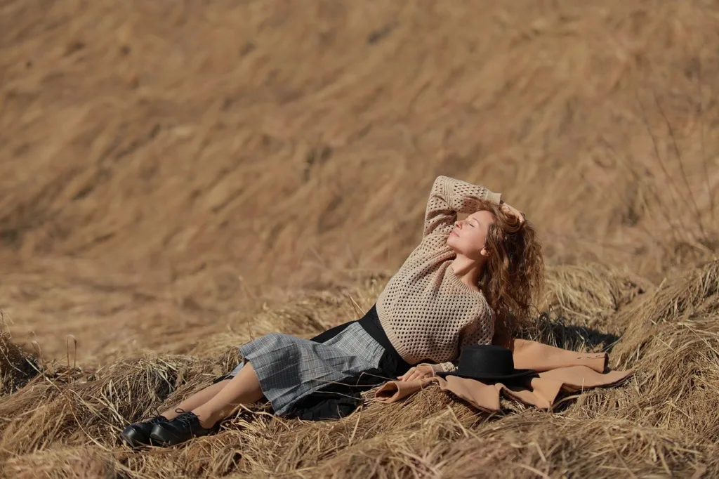 uma jovem de vestido e calçado, deitada obre o feno, se expondo a luz do sol.