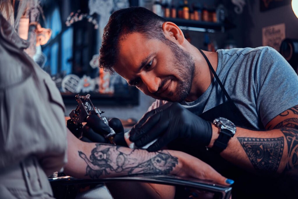 um jovem tatuador de luvas pretas, tatuando um braço.