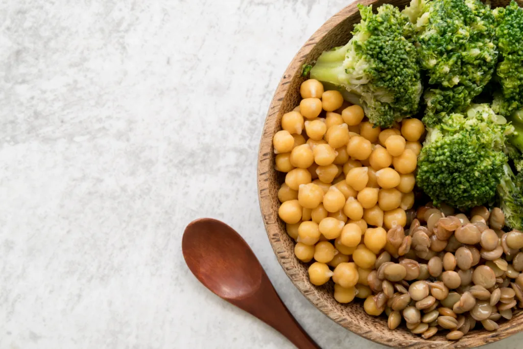 tigela de madeira contendo grão de bico, feijão e brócolis.