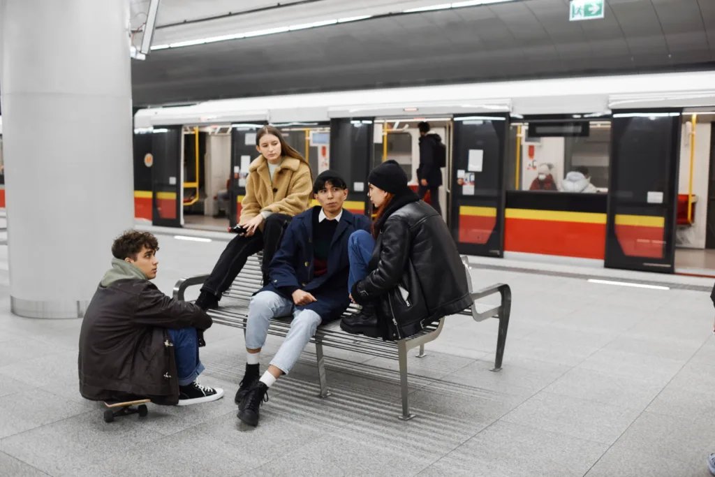 grupo de jovens sentados em um banco numa estação de metro.