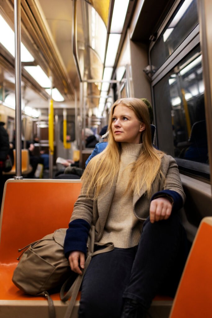 uma jovem mulher loira sentada em um banco do vagão de  metro com sua bolsa ao lado.