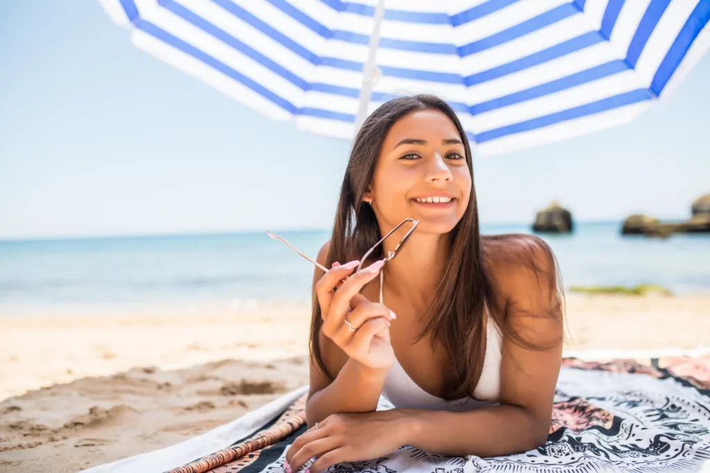 uma jovem deitada  de bruços na praia sobre um guarda sol.  