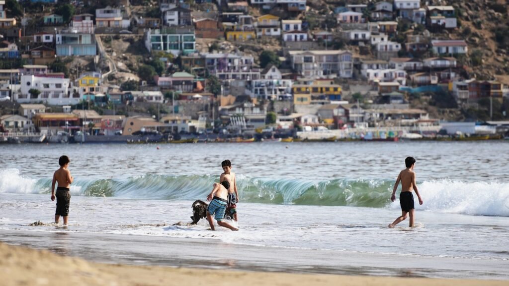 criancas jogando bola na praia, proximo a agua.