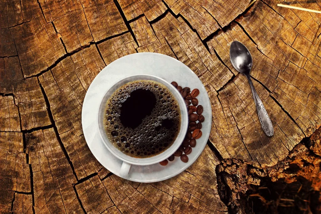 xicara de café sobre uma mesa de madeira natural, com grãos de café no pires.