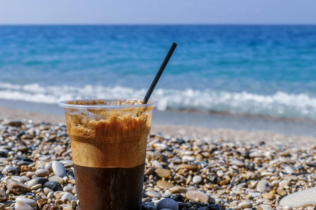 uma xicara de uma bebida  a base de café, numa mesa em frente a uma praia.