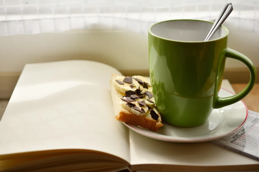 um livro aberto, com ima xicara de café e uma barra de cereal.