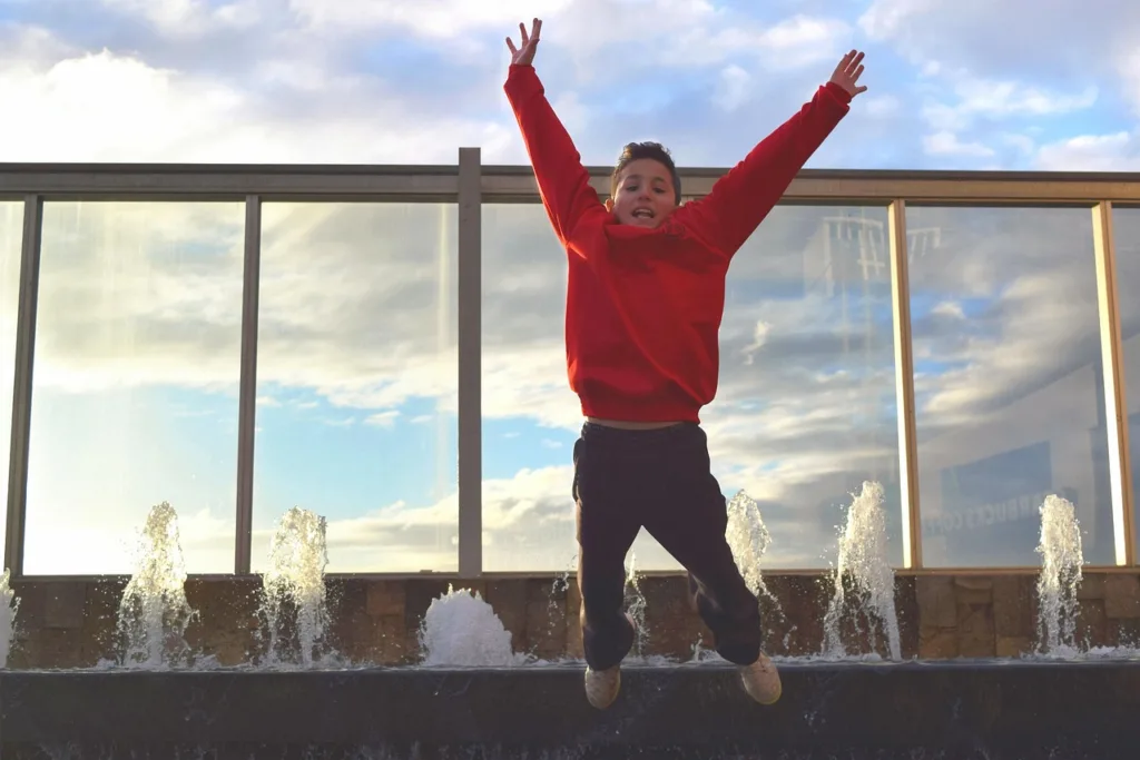 menino de blusa vermelha saltando ao ar livre.