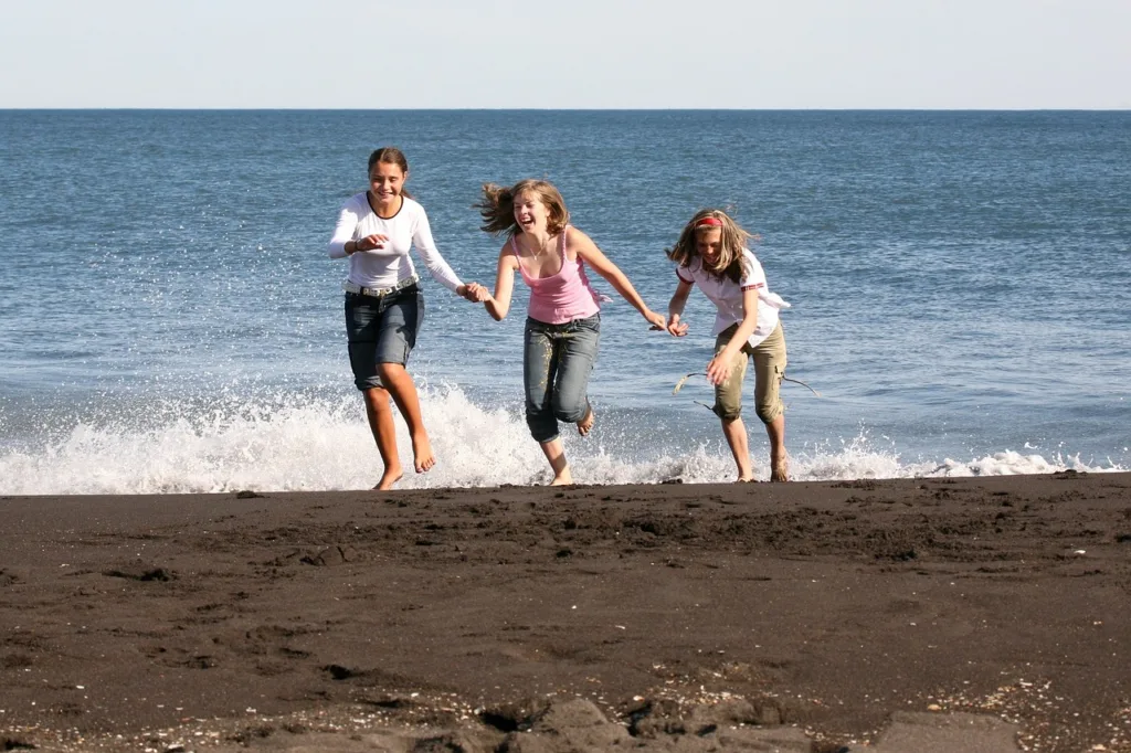 três jovens vestidos com roupas casuais  molhando os pés nas ondas de uma praia.