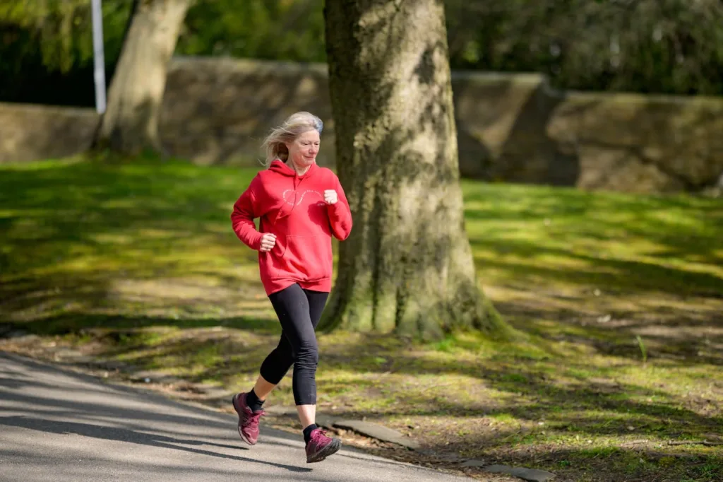 mulher acima dos 50 anos, com roupa de jogging, correndo ao ar livre.