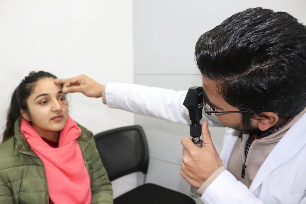 um medico fazendo exame de retinoscopia em uma jovem sentada em uma cadeira.
