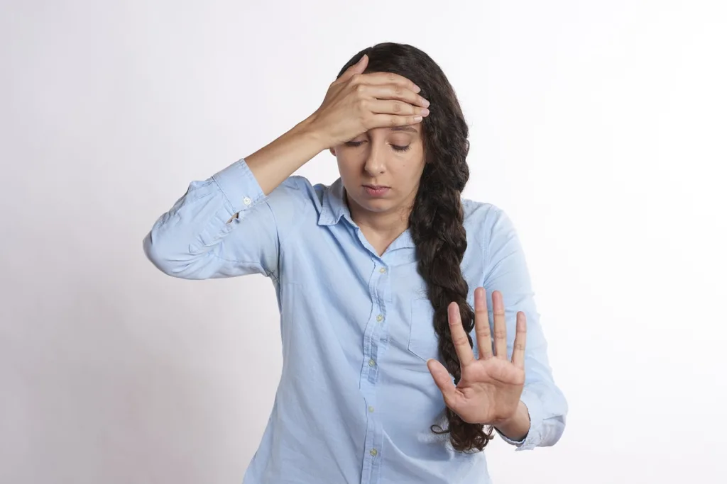 mulher de tranças com uma mão na testa pedindo um tempo para raciocinar.