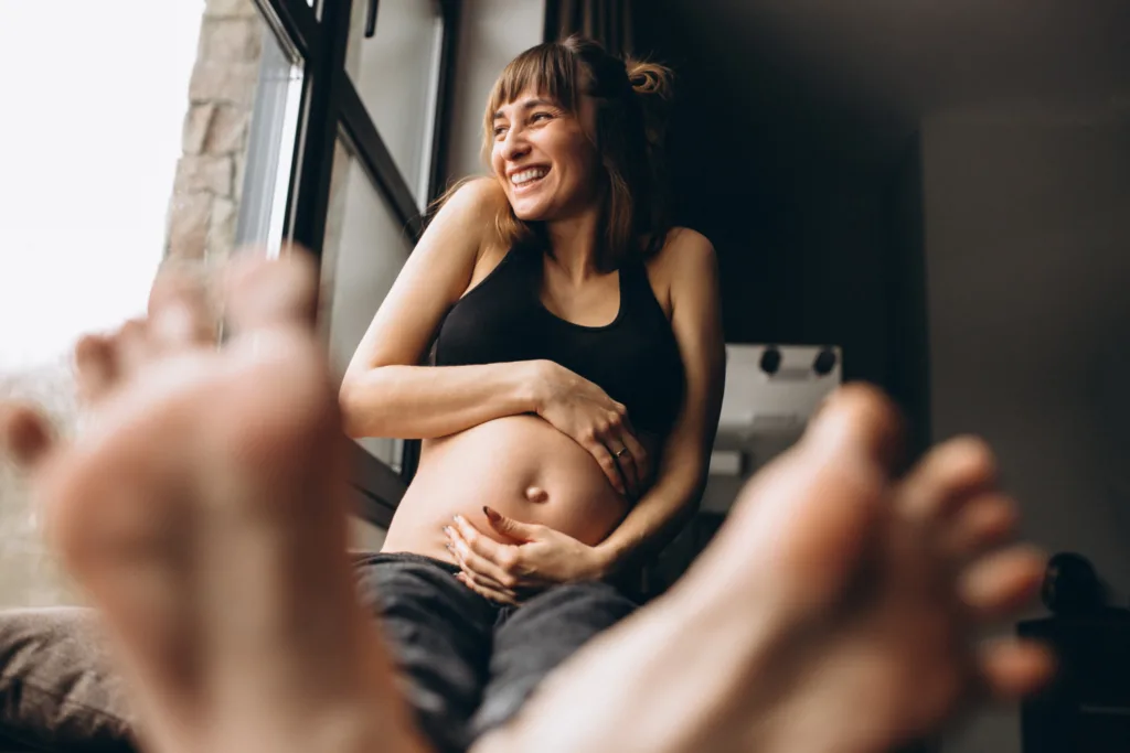 uma gravida sentada na janela, sorridente.