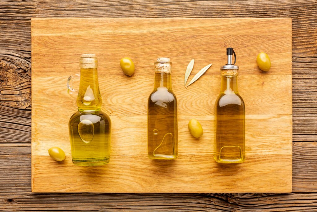 três vidros de azeite de olivas deitados numa tabua de madeira com algumas azeitonas  sobre ela.