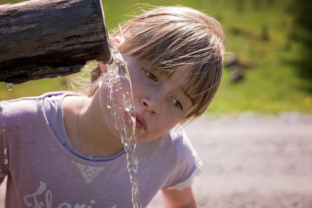 uma menina bebendo agua em uma bica ao ar livre.