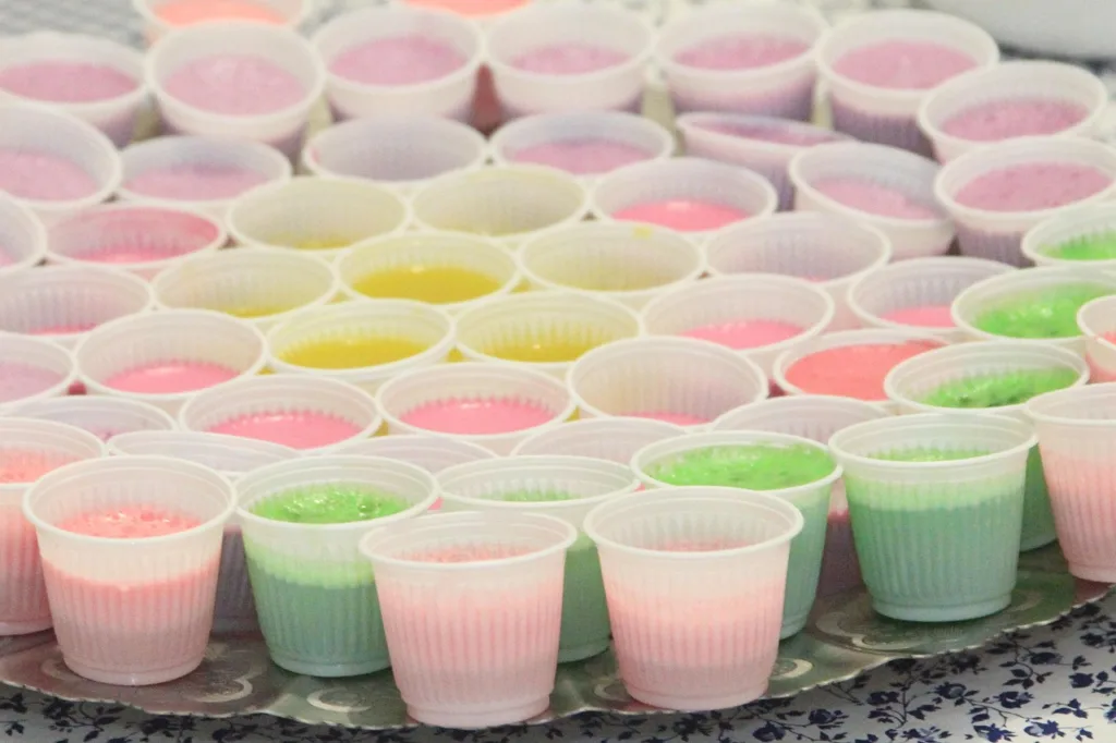 bandeja com vários copinhos de varias cores de gelatinas. 