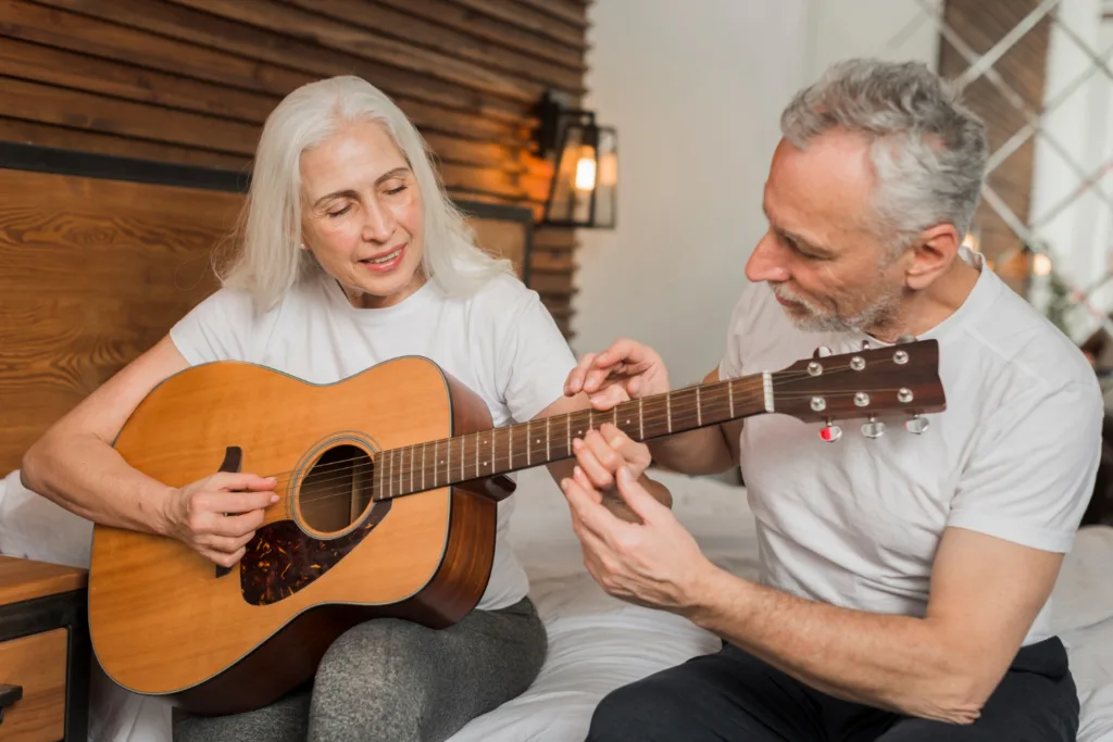 uma mulher idosa, aprendendo a tocar violão com um professor.