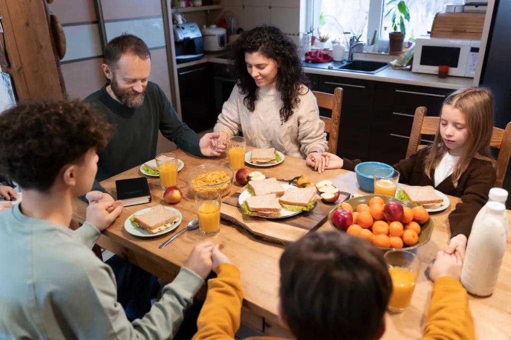 Família unida de mãos dadas fazendo uma oração antes de comer.