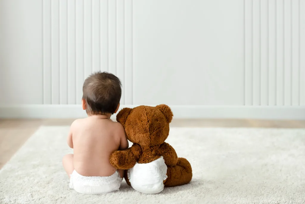 foto de um bebê abraçado com um ursinho de pelúcia, visto por trás.