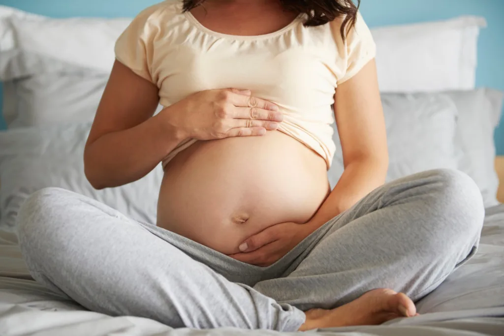 uma gravida sentadda com as pernas cruzadas, acariciando a barriga.