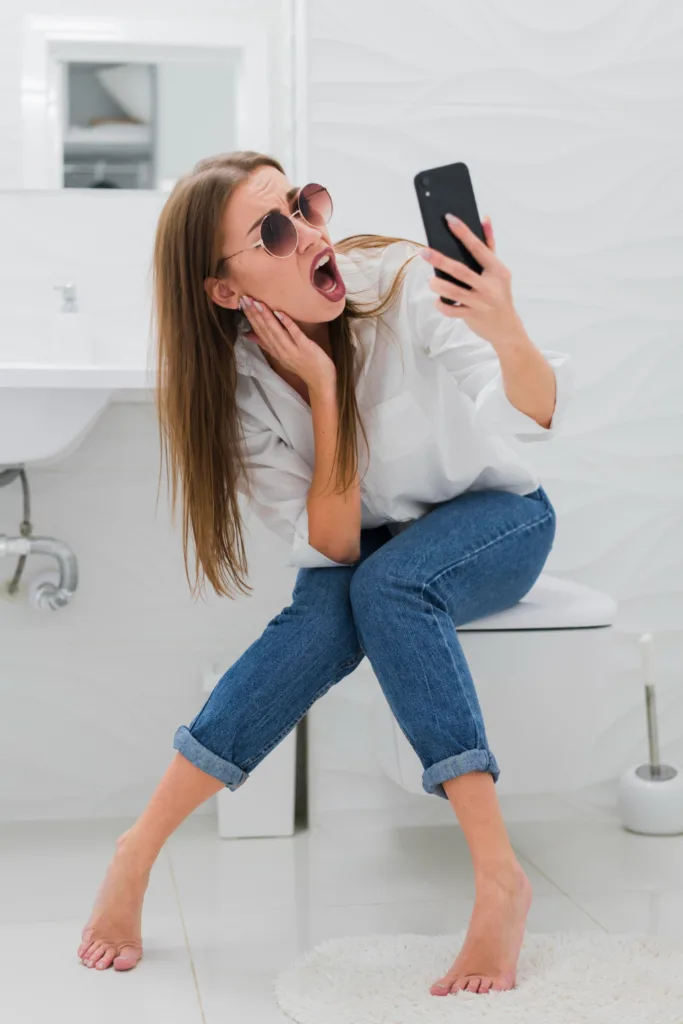 uma jovem sentada num vaso sanitario usando um celular.