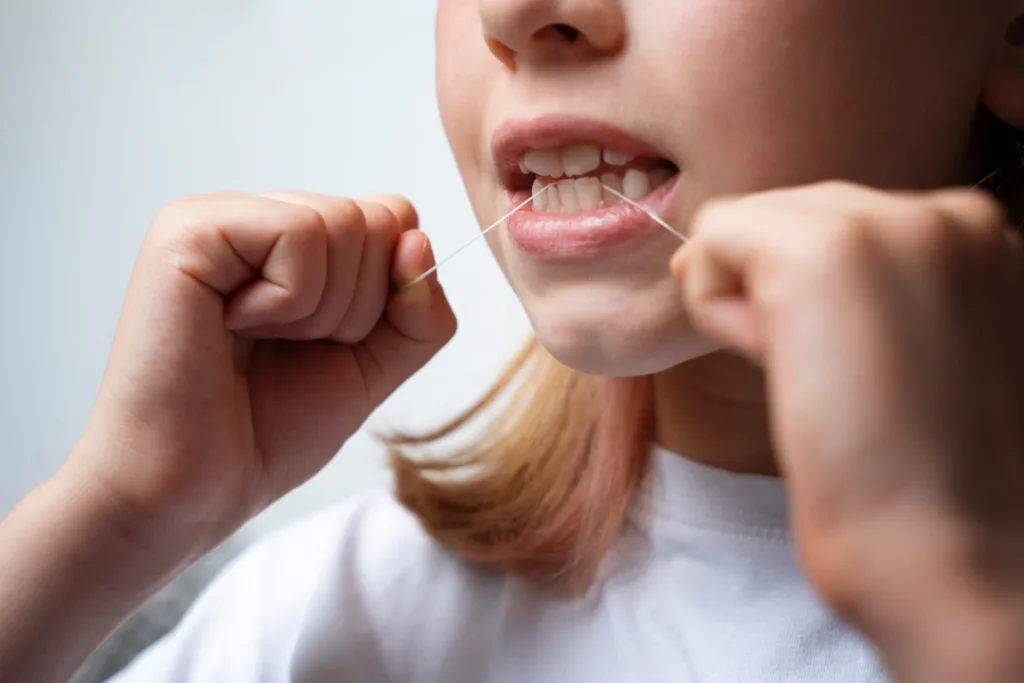 close da boca de uma jovem usando fio dental.