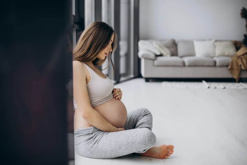 gravida sentada no chão da sala, com as pernas cruzadas, acariciando a barriga.