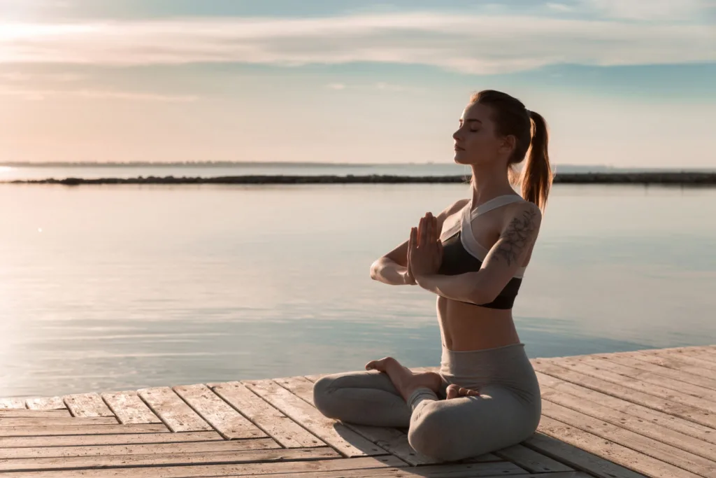 mulher meditando a margem de um lago.